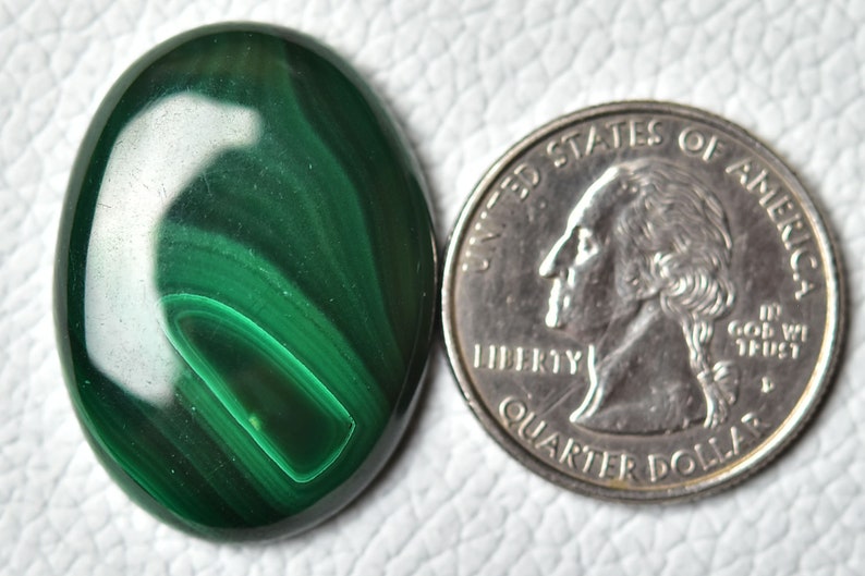 May include: A green malachite cabochon, oval shaped, with a swirling pattern. The cabochon is about the size of a US quarter.