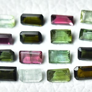 Op de afbeelding: Assortiment van 15 groene, zwarte en roze edelstenen geslepen in een rechthoekige vorm. De edelstenen zijn gerangschikt in drie rijen van vijf.