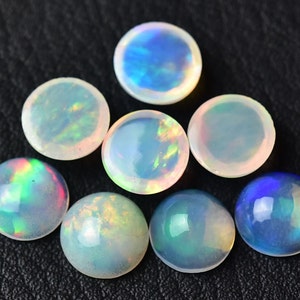 Pode incluir: Uma cole&ccedil;&atilde;o de oito caboch&otilde;es de opala redondos em v&aacute;rios tons de branco, azul e verde. As opalas s&atilde;o iridescentes e t&ecirc;m uma superf&iacute;cie lisa e polida.