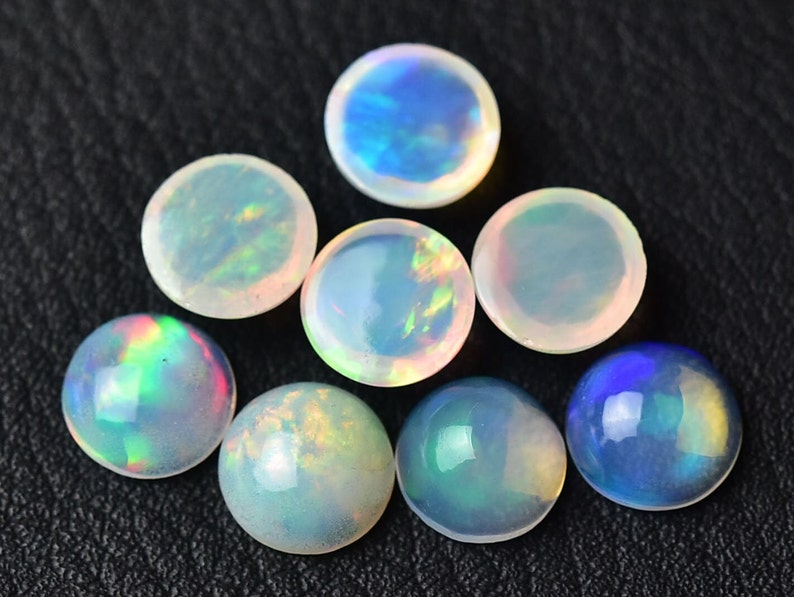 Pode incluir: Uma cole&ccedil;&atilde;o de oito caboch&otilde;es de opala redondos em v&aacute;rios tons de branco, azul e verde. As opalas s&atilde;o iridescentes e t&ecirc;m uma superf&iacute;cie lisa e polida.