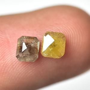 May include: Two emerald cut rough diamonds, one is a light brown color and the other is a yellow color.