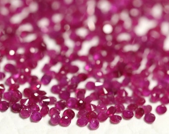 May include: A close-up view of a pile of loose, faceted ruby gemstones. The rubies are a deep, rich red color and have a high shine.