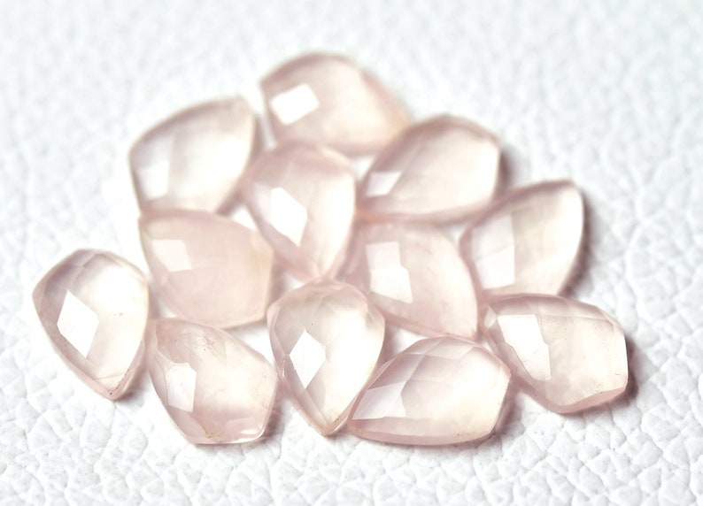 May include: A collection of pale pink, faceted, teardrop-shaped gemstone beads.