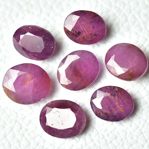 May include: Seven oval-shaped pink gemstones with a faceted cut. The gemstones have a pink hue with a slight orange tint.