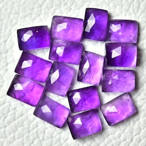 Peut inclure: Une collection de 12 pierres précieuses d'améthyste facettées de forme rectangulaire. Les pierres sont d'une couleur violet foncé et ont une finition polie.