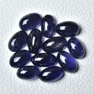 May include: A group of 12 oval-shaped, deep blue gemstones. The gemstones are smooth and polished, with a slight sparkle.