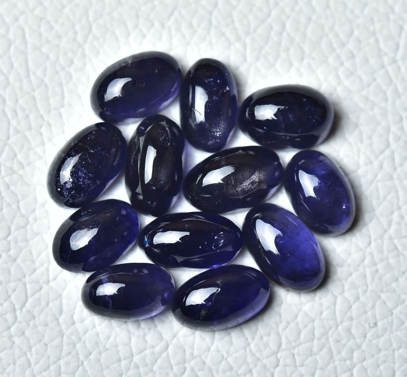 May include: A group of 12 oval-shaped, deep blue gemstones. The gemstones are smooth and polished, with a slight sparkle.