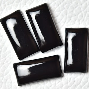 May include: Four black rectangular cabochon gemstones with a glossy finish.