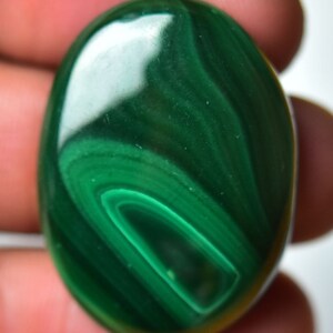 May include: A smooth, oval-shaped malachite gemstone with a deep green color and swirling patterns.