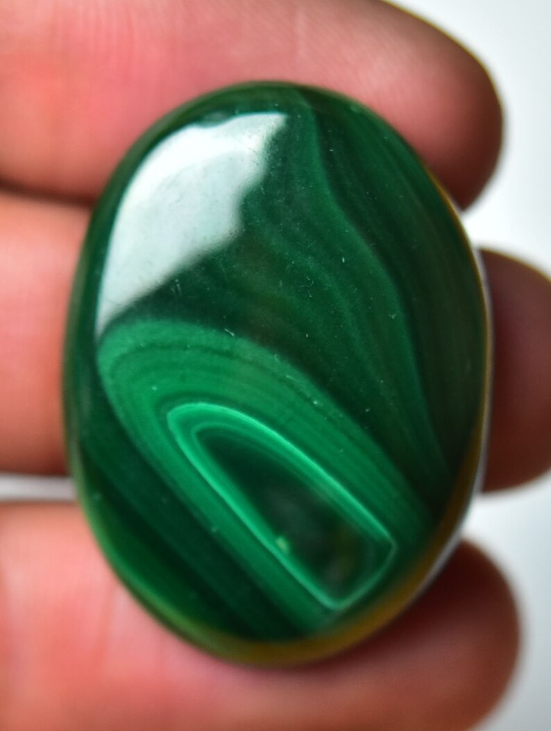 May include: A smooth, oval-shaped malachite gemstone with a deep green color and swirling patterns.