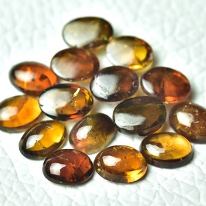 May include: A collection of 15 oval-shaped gemstones in shades of brown, gold, and green. The stones are smooth and polished, with a slight shimmer.