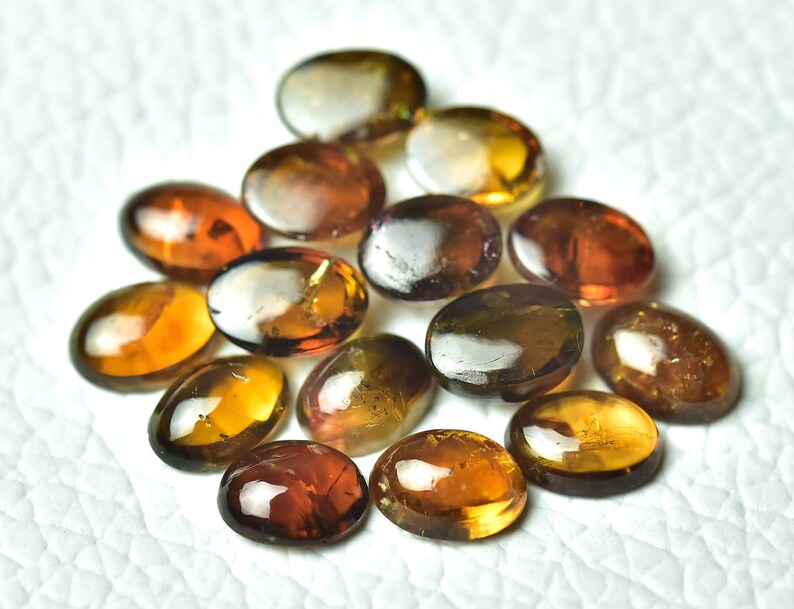May include: A collection of 15 oval-shaped gemstones in shades of brown, gold, and green. The stones are smooth and polished, with a slight shimmer.
