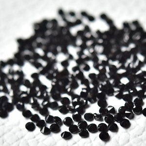 May include: A pile of black round gemstones, likely black diamonds, on a white surface.