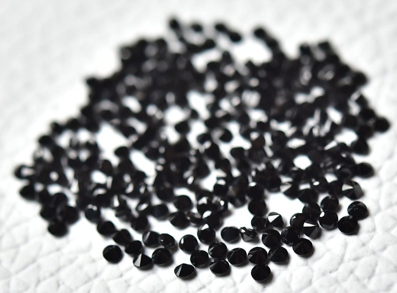 May include: A pile of black round gemstones, likely black diamonds, on a white surface.