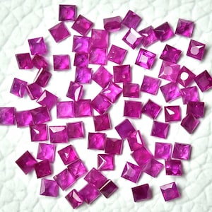 Puede incluir: Una colección de piedras preciosas cuadradas de color rosa. Las piedras preciosas están esparcidas sobre una superficie blanca.