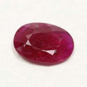 May include: A deep red oval-shaped gemstone with a faceted cut. The gemstone has a slightly cloudy appearance.