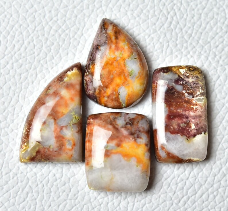 May include: Five polished gemstone cabochons in various shapes and sizes. The stones are a mix of white, brown, and orange with a marbled pattern.