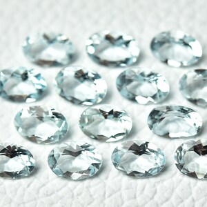 May include: A collection of oval-shaped aquamarine gemstones, each with a light blue hue and a smooth, polished finish.