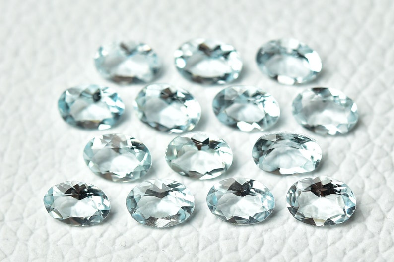 May include: A collection of oval-shaped aquamarine gemstones, each with a light blue hue and a smooth, polished finish.