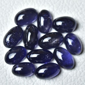 May include: A collection of twelve oval-shaped, dark blue gemstones. The stones are smooth and polished, with a slight sheen.