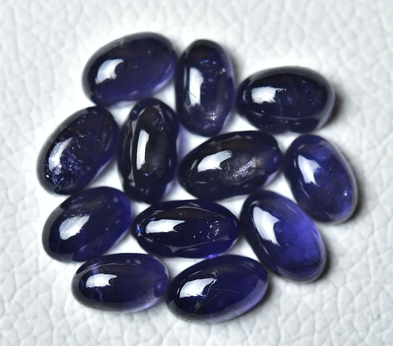 May include: A collection of twelve oval-shaped, dark blue gemstones. The stones are smooth and polished, with a slight sheen.