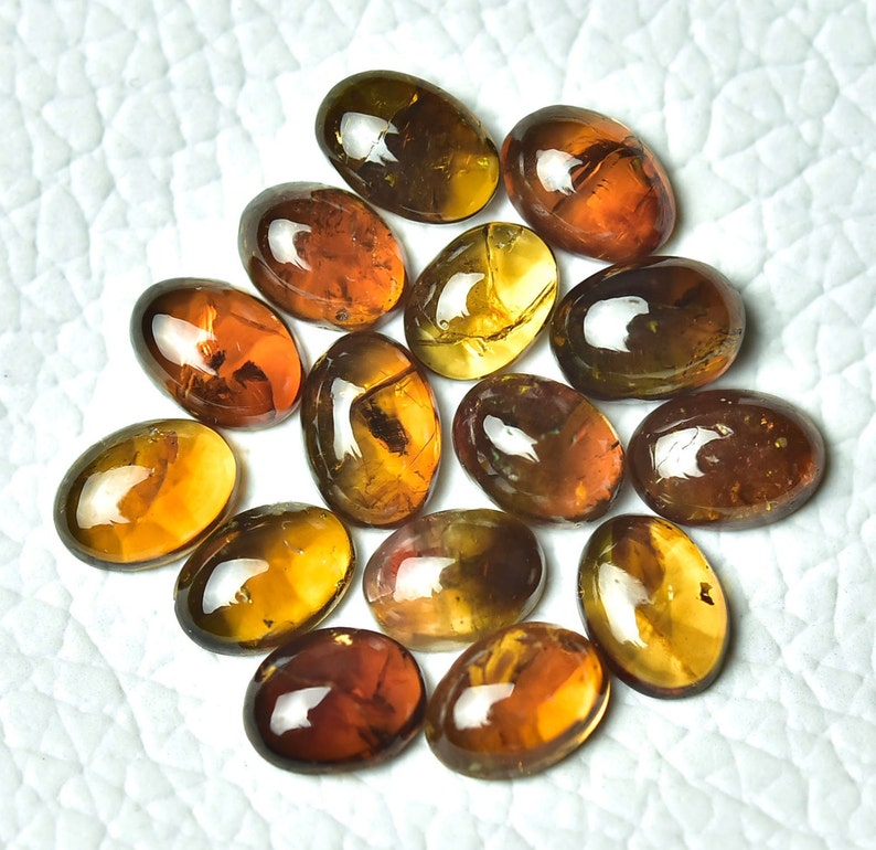 May include: A collection of 15 oval-shaped, translucent gemstones with a variety of brown and yellow hues. The stones have a glossy finish and appear to be cut and polished.