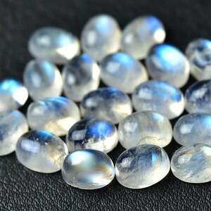 May include: A collection of oval-shaped moonstone cabochons, with a milky white color and iridescent blue flashes.