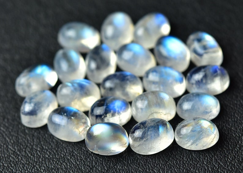 May include: A collection of oval-shaped moonstone cabochons, with a milky white color and iridescent blue flashes.