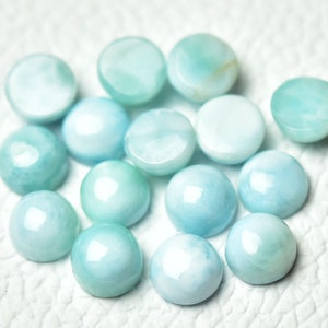 Puede incluir: Una colecci&oacute;n de 14 piedras preciosas cabuj&oacute;n de color azul claro, cada una con un patr&oacute;n &uacute;nico de remolino. Las piedras son lisas y pulidas, con un ligero brillo iridiscente.