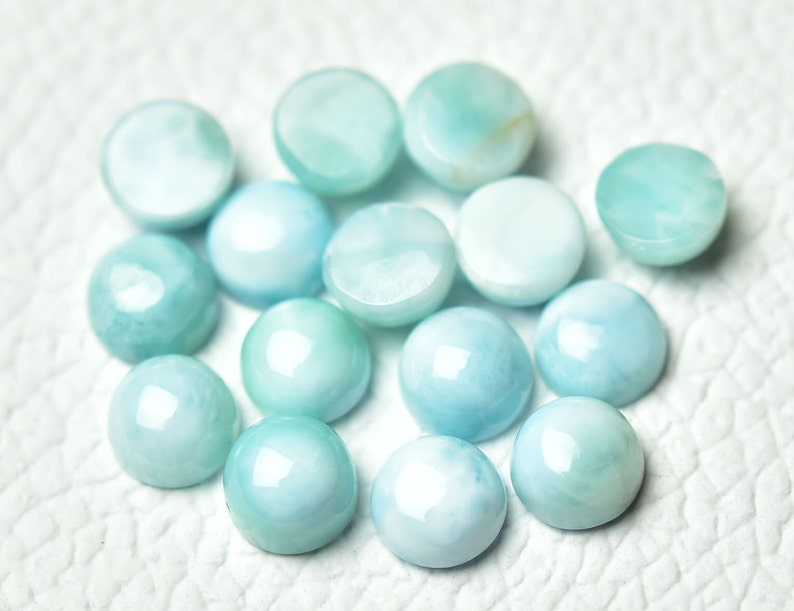 Puede incluir: Una colecci&oacute;n de 14 piedras preciosas cabuj&oacute;n de color azul claro, cada una con un patr&oacute;n &uacute;nico de remolino. Las piedras son lisas y pulidas, con un ligero brillo iridiscente.