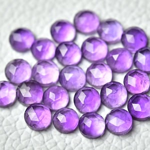May include: A collection of 20 faceted amethyst gemstones in various shades of purple. The stones are round and have a smooth, polished finish.