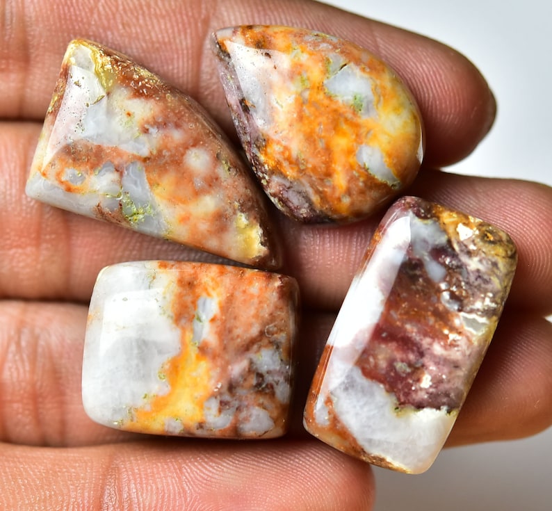 May include: Four polished, white, brown, and orange agate cabochons with a variety of patterns and textures.