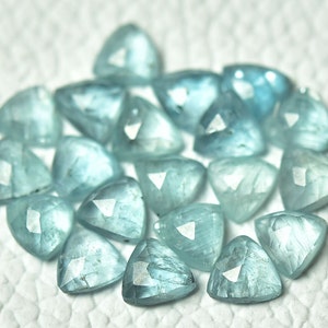 May include: A group of 20 light blue aquamarine gemstone triangle shaped beads. The beads are faceted and have a translucent appearance.