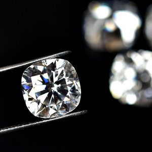 Könnte beinhalten: Ein großer, klarer, runder Diamantenstein, der in einer Pinzette vor einem schwarzen Hintergrund gehalten wird. Der Diamant hat viele Facetten und reflektiert das Licht.