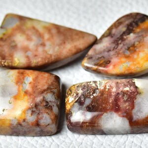 May include: Four polished agate cabochons in various shapes and sizes. The stones feature a mix of white, brown, orange, and red colors with a swirling pattern.