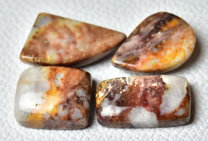 May include: Four polished agate cabochons in various shapes and sizes. The stones feature a mix of white, brown, orange, and red colors with a swirling pattern.