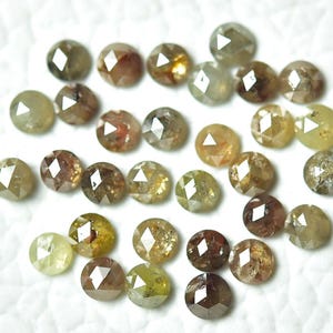 Op de afbeelding: Een verzameling van 25 losse, gefacetteerde, ronde, natuurlijke diamanten. De diamanten zijn een mix van bruin, groen en geel. De diamanten zijn ongeveer 3 mm in diameter.