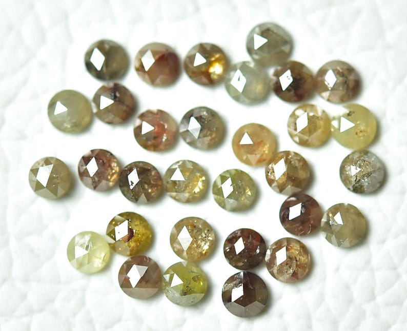 Op de afbeelding: Een verzameling van 25 losse, gefacetteerde, ronde, natuurlijke diamanten. De diamanten zijn een mix van bruin, groen en geel. De diamanten zijn ongeveer 3 mm in diameter.