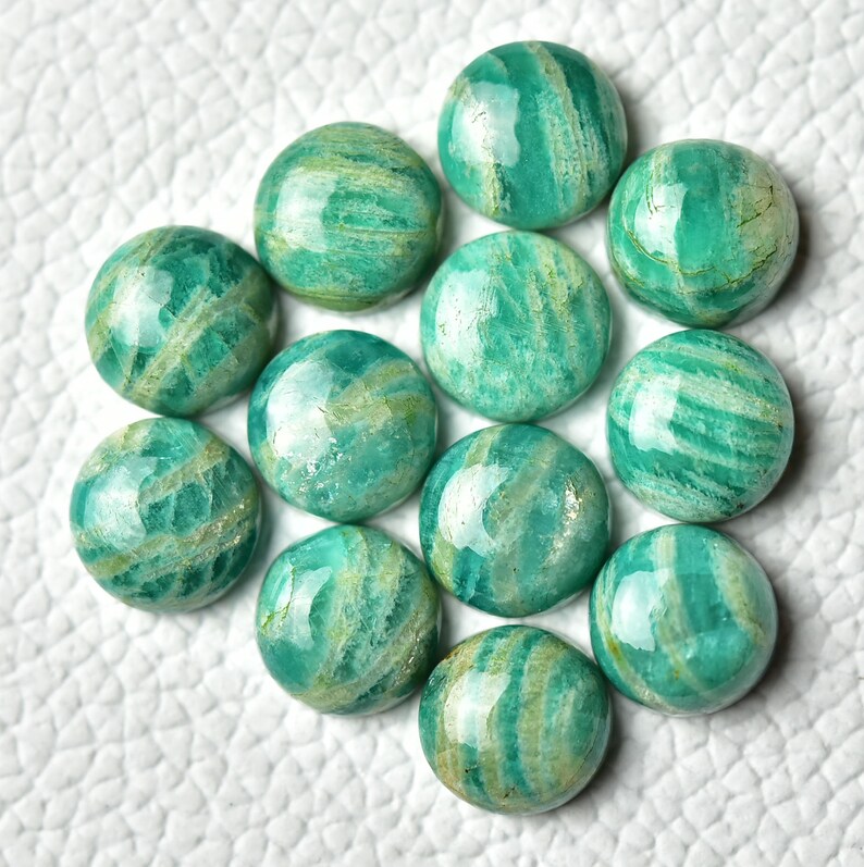 May include: A collection of 14 green and white amazonite cabochons, each with a unique pattern of striations. The cabochons are smooth and polished, with a glossy finish.