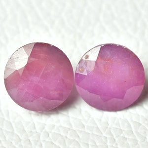 Könnte beinhalten: Zwei rosa runde facettierte Edelsteine auf weißem Hintergrund.