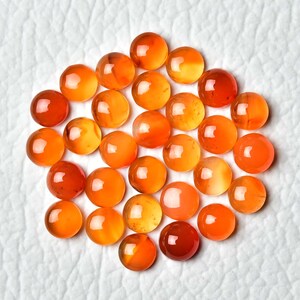 Pu&ograve; includere: Una collezione di pietre preziose rotonde e lucide nelle tonalit&agrave; dell'arancione e del rosso. Le pietre sono disposte vicine, creando un gruppo di globi traslucidi e vibranti. Le pietre hanno una superficie liscia e riflettente.