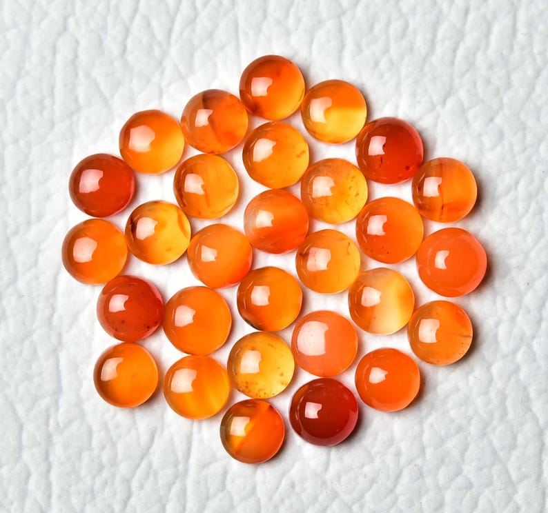 Pu&ograve; includere: Una collezione di pietre preziose rotonde e lucide nelle tonalit&agrave; dell'arancione e del rosso. Le pietre sono disposte vicine, creando un gruppo di globi traslucidi e vibranti. Le pietre hanno una superficie liscia e riflettente.