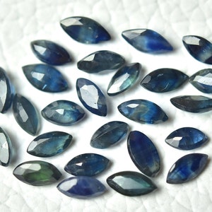 Op de afbeelding: Een verzameling van 20 blauwe saffier edelstenen in marquise-vorm. De saffieren zijn gefacetteerd en hebben verschillende tinten blauw.