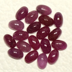 Puede incluir: Una colección de 20 piedras preciosas de rubí talladas en forma ovalada. Los rubíes son de color rojo intenso con un ligero tono púrpura. Las piedras son de diferentes tamaños y formas, pero todas están pulidas y lisas.
