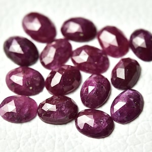 May include: A collection of 15 faceted ruby gemstones in various sizes and shades of pink and red. The gemstones are oval shaped and have a polished finish.