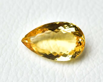 May include: A faceted, pear-shaped gemstone with a vibrant yellow hue. The gem's cut reveals multiple facets, creating a sparkling effect. The gemstone is set against a white background.