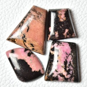 May include: Four pink and black rhodochrosite cabochons, cut and polished for jewelry making. The stones have a unique marbled pattern with pink and black swirls.