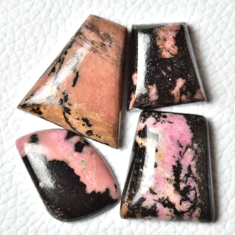 May include: Four pink and black rhodochrosite cabochons, cut and polished for jewelry making. The stones have a unique marbled pattern with pink and black swirls.