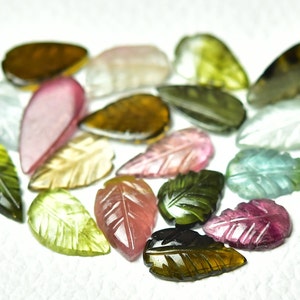May include: Assortment of carved gemstone leaves in various colors, including green, pink, brown, and clear. The leaves are all carved in a similar leaf shape and have a smooth, polished finish.