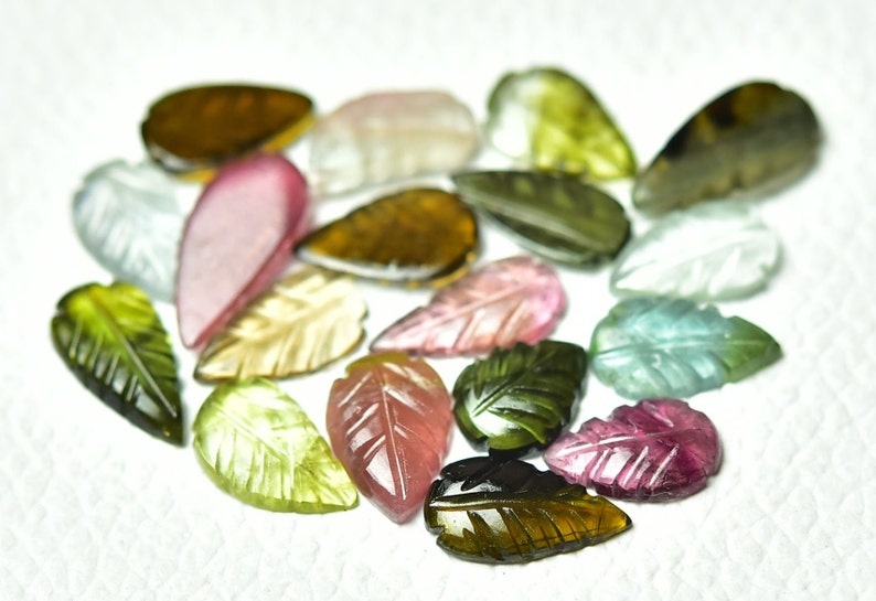 May include: Assortment of carved gemstone leaves in various colors, including green, pink, brown, and clear. The leaves are all carved in a similar leaf shape and have a smooth, polished finish.